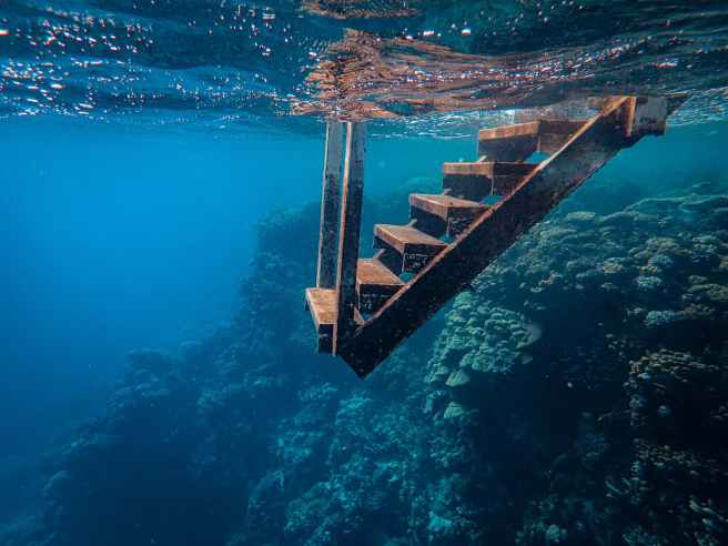 Rusted stairs lead from the water's surface into an undersea reef.