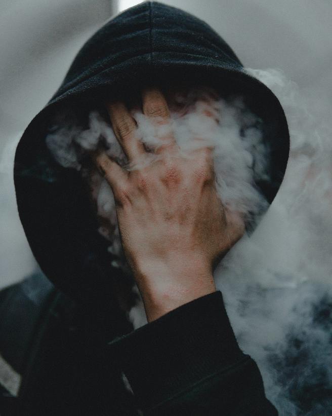 Writer in motion prompt shows what appears to be a hooded figure, face hidden behind a splayed masculine-looking hand, with thick smoke curling out between his fingers.