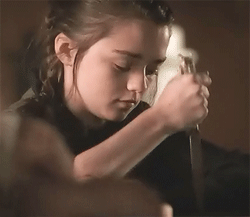 Arya Stark of Game of Thrones stabs a table with a very focused expression.