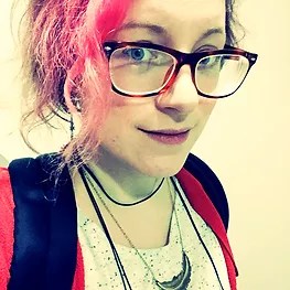 Photo of Ren Hutchings, an enby author with pink hair, glasses, and a slight smile