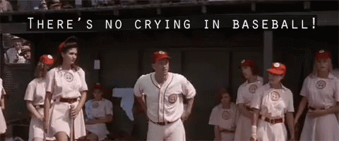 A man in a ball cap and white uniform spreads his arms and says "There's no crying in baseball!" while women baseball players look askance at him.